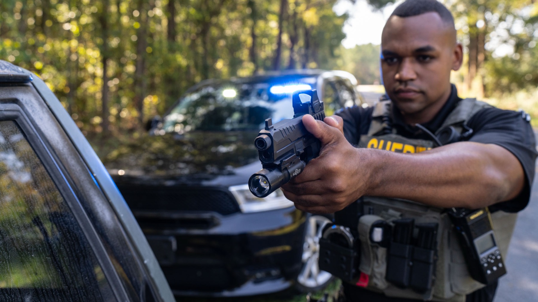 Deputy aiming pistol beside patrol car